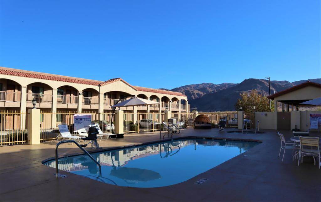 Outdoor swimming pool next to a motel with mountains in the background.
